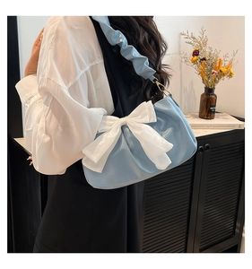 Detail of light blue shoulder bag featuring a large white bow and pleated strap