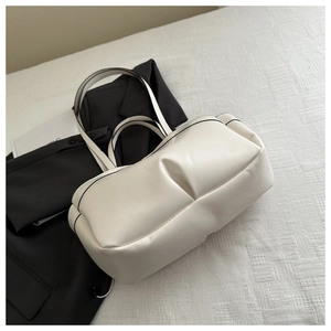 Close-up of cream pleated leather tote bag with black edge detailing on textured surface