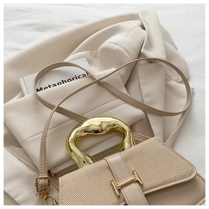 Detail of cream shoulder bag with woven flap texture and chunky gold metal handle