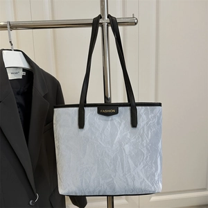 Minimalist silver pleated tote bag with black handles and fashion metal plaque on white wall