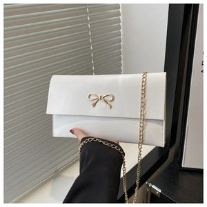 Close-up of a white leather crossbody bag with a delicate gold metal bow and chain strap