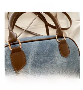 Detail of denim Boston bag featuring brown leather handles and golden hardware