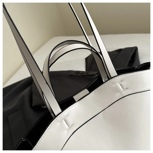 Detail shot of black contrast stitching and handle joints on a white leather tote bag