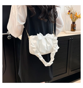 Detail of white shoulder bag with a large bow, ruffled strap and gold chain link