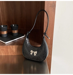 Detail of black leather hobo bag with crocodile texture and gold bow metal accent