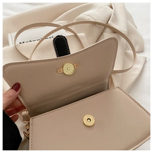 Close-up of a cream leather handbag featuring a golden magnetic closure and sleek strap