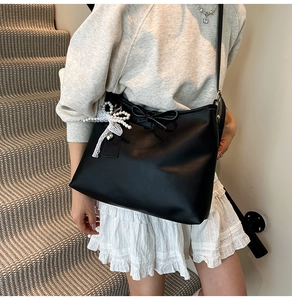 Close-up of black leather tote bag with elegant bow detail and pearl heart charm