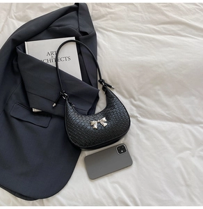 Close-up of black crocodile-embossed crescent bag with silver metallic bow detail