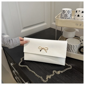 Detail of white leather shoulder bag featuring a gold bow clasp and sleek chain strap