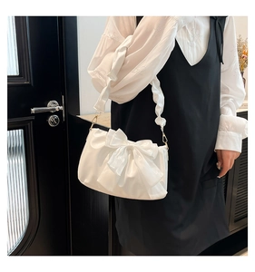 Detail of white pleated shoulder bag with a large satin bow and metallic accents