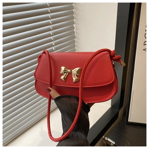 Détail d'un sac bandoulière en cuir rouge avec boucle en métal doré en forme de nœud chic