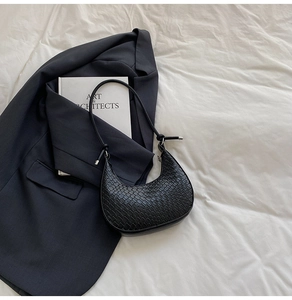 Detail of black croissant shoulder bag with crocodile texture and metal buckle on fabrics