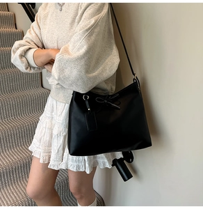Close-up of black tote bag with decorative bow and leather tag on a model at stairs