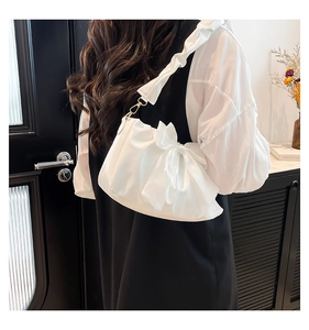 Detail of white pleated shoulder bag with large bow and silky texture on a model