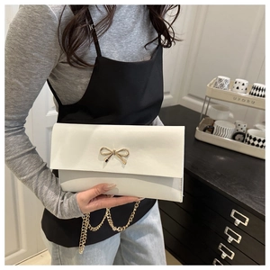 Detail of white envelope bag with gold bow clasp and metallic chain strap on dark background
