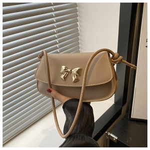 Détail du sac bandoulière beige avec fermoir en métal doré en forme de nœud et sangle nouée