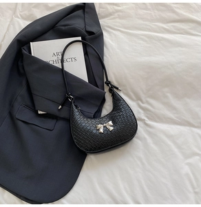 Detail of black croc-embossed hobo bag featuring a silver metal bow on a dark blazer