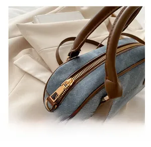 Detailed close-up of smooth gold zipper and leather handles on denim bowling bag