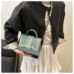 Detail of mint green crocodile pattern handbag with elegant metal chain strap and top handle