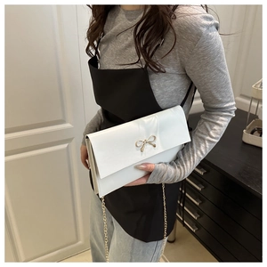 Close-up of white envelope bag with golden bow and elegant metal chain strap