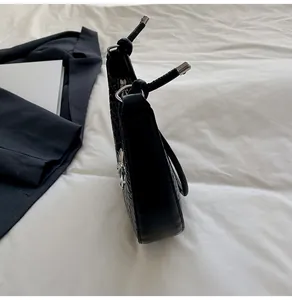Detail of black woven crescent bag with silver bow ornament on white bedding