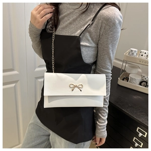 Chic white envelope chain bag with gold bow clasp, shown as a shoulder carry detail