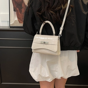 Elegant beige croc-embossed shoulder bag with metallic lock shown on a model