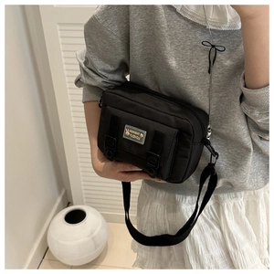 Detail view of the black nylon crossbody bag featuring stylish front buckles and adjustable strap