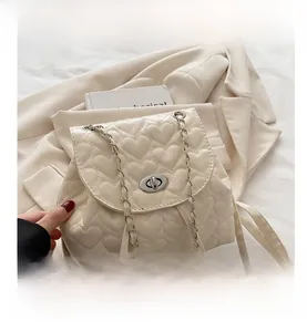 Macro shot of cream heart-quilted texture with silver twist lock and chain strap