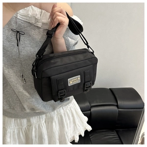 Detail van zwarte nylon crossbody tas met dubbele gespbanden en verstelbare schouderriem