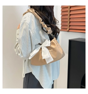 Detail of beige pleated shoulder bag featuring a large white bow and a ruffled strap