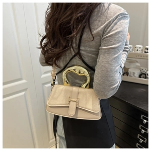 Detail of beige crossbody bag with unique gold metal handle and textured flap closure