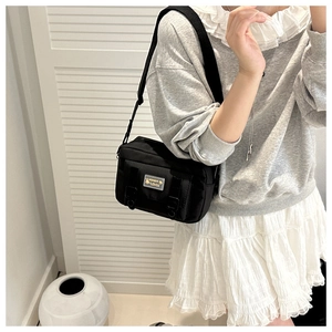 Fashionable black nylon crossbody bag featuring double buckles and metallic label detail