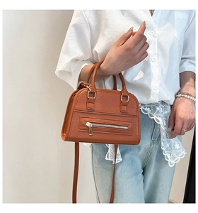 Detail view of orange-brown pebble leather Boston bag with metal zipper and dual handles