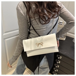 Detail of elegant cream envelope crossbody bag featuring a gold bow clasp and chain strap