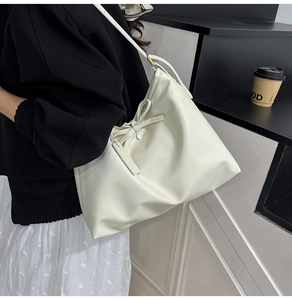 Detail of cream white tote bag with large 3D bow design and glossy leather finish