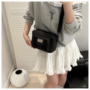 Detail of a black crossbody square bag with a metal tag and decorative double straps
