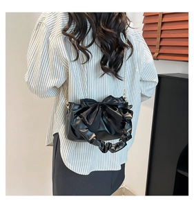 Detail of black pleated shoulder bag with large bow and golden chain strap for women