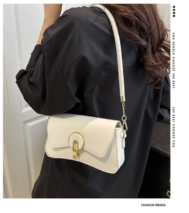 Detail of cream shoulder bag with golden ring buckle shown on black clothing background
