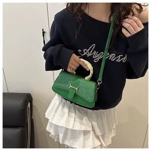 Detail of emerald green mini bag with sequins and curved gold metal handle on model