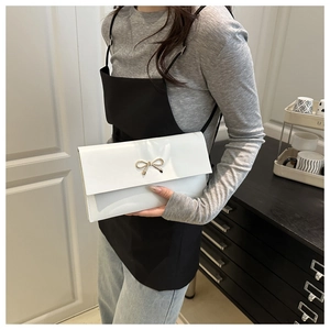 Detail of white leather crossbody bag with a golden metal bow buckle on the flap