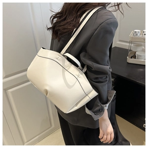 Detail view of cream tote bag with black piping and slender shoulder straps shown on model