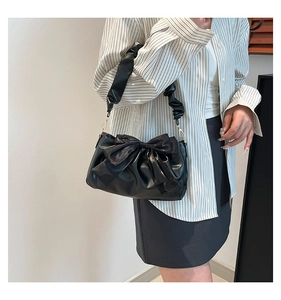 Detail of black bow shoulder bag featuring a ruched cloud strap and golden buckle accents