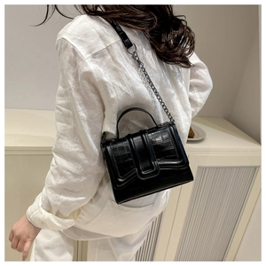 Détail d'un mini sac à main noir gaufré crocodile avec bandoulière porté par un mannequin