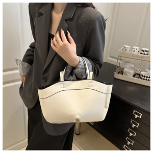 Close-up of a stylish cream tote bag with black trim held by a model in a gray blazer
