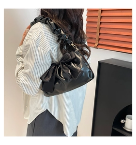 Detail of black faux leather shoulder bag featuring large bow and ruched strap design