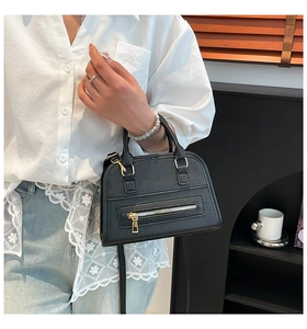 Detail of black pebbled leather Boston bag with gold hardware worn by a model