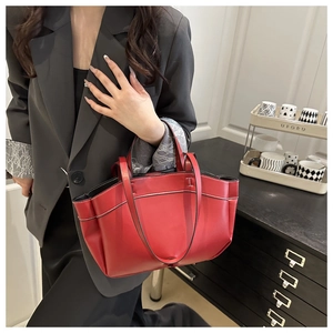 Close-up of red leather tote bag showing white contrast stitching and dual carry handles