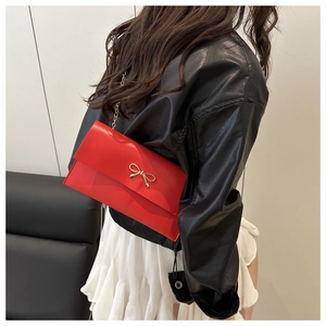 Detail of red envelope bag featuring a gold bow accent and a sleek metal chain strap