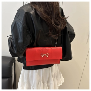 Detail view of a red envelope chain bag with a gold bow buckle on a model in a black jacket